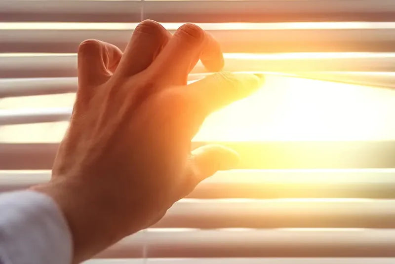 Sonnenstrahlen durchleuchten eine Jalousie.