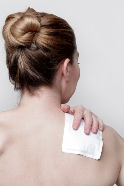 Une femme utilise un patch chauffant pour soulager une douleur à l’épaule