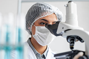 Mujer con mascarilla mirando por un microscopio texto alternativo